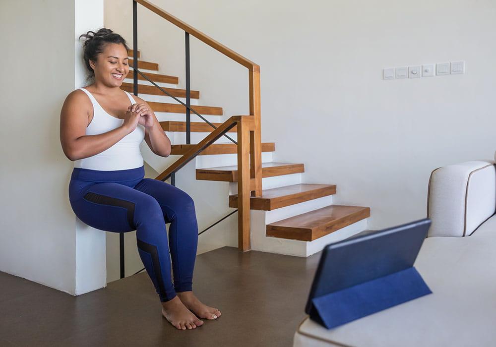 Woman practicing squats against a wall at home